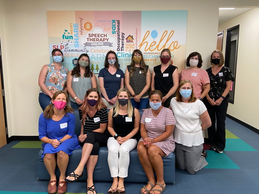 12 women wearing masks standing and sitting in front of the hello clinic mural 